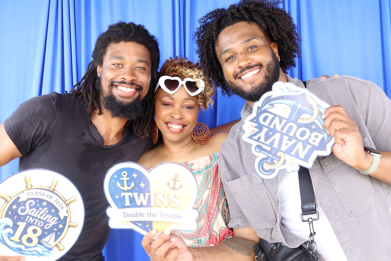Three guests holding graduation and twins props in front of a blue backdrop