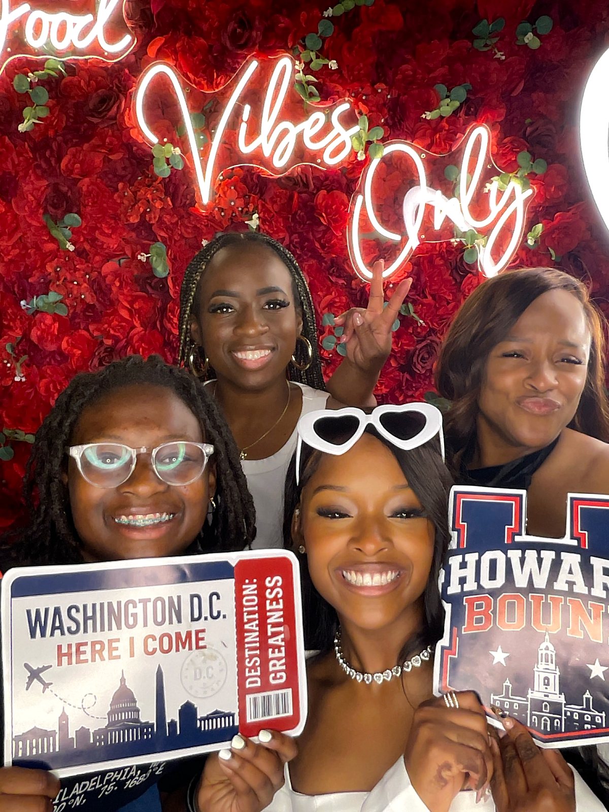 Four guests posing with college-bound signs in front of a red floral Good Vibes Only backdrop