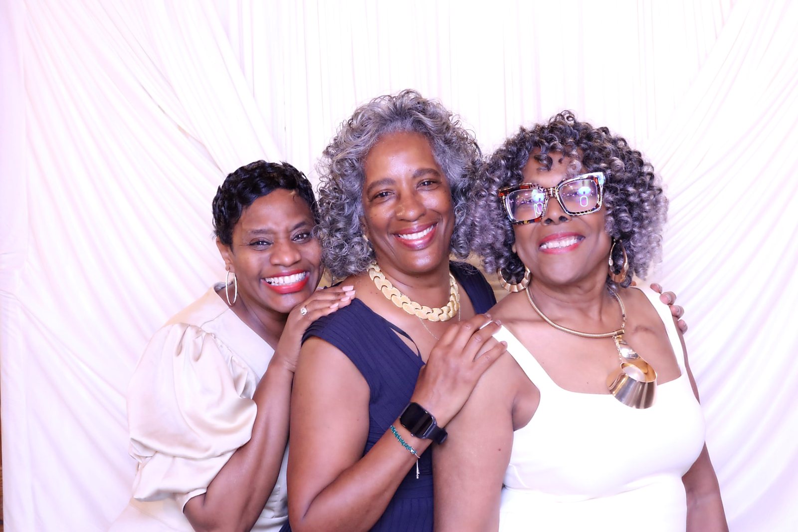 Three women laughing together in front of a white draped backdrop