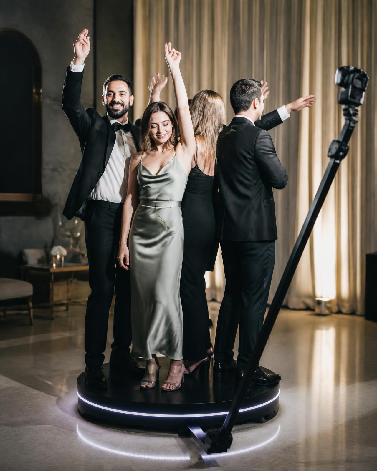 Wedding guests raising their arms on a lit 360 video booth platform as the camera arm sweeps around them