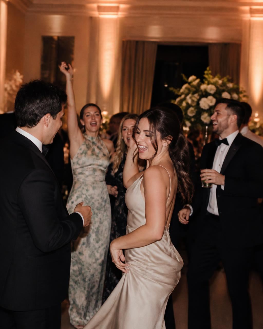 Wedding guests dancing and cheering under warm uplighting on the reception dance floor